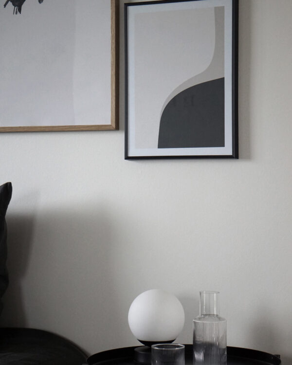 A white wall with a black thin frame hanging on the wall with an art print inside with the title Right Here 02