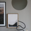 A light brown wall with an oak frame with the art print; Right Here 04 inside. A black minimal sculpture is partly in front of the frame.