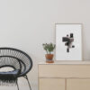 oak frame with black minimal art print standing on furniture next to a black chair