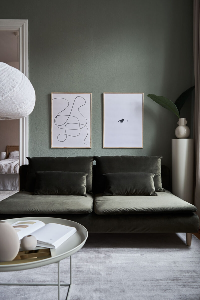 a living room with dark green walls and couch with two art prints on the wall with the title; The Pen 02 and The Dot