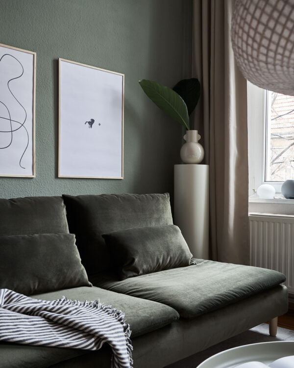 a living room with dark green walls and couch with two art prints on the wall with the title; The Pen 02 and The Dot