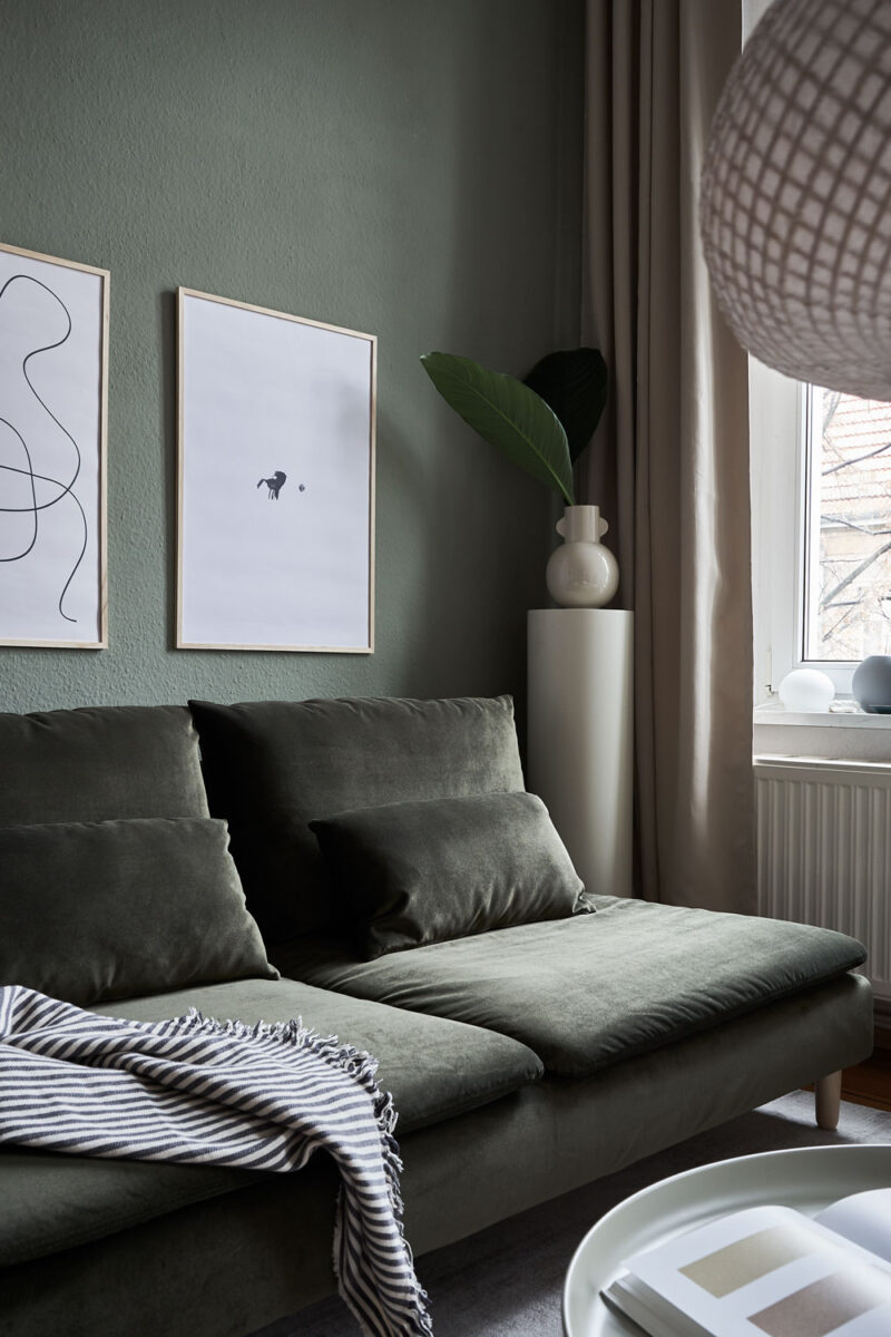 a living room with dark green walls and couch with two art prints on the wall with the title; The Pen 02 and The Dot