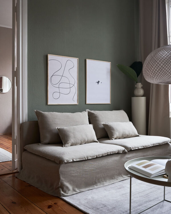 a living room with dark green walls and a beige couch with two art prints on the wall with the title; The Pen 02 and The Dot