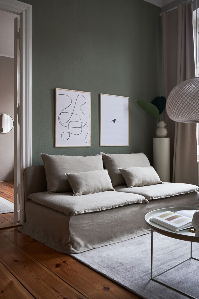 a living room with dark green walls and a beige couch with two art prints on the wall with the title; The Pen 02 and The Dot