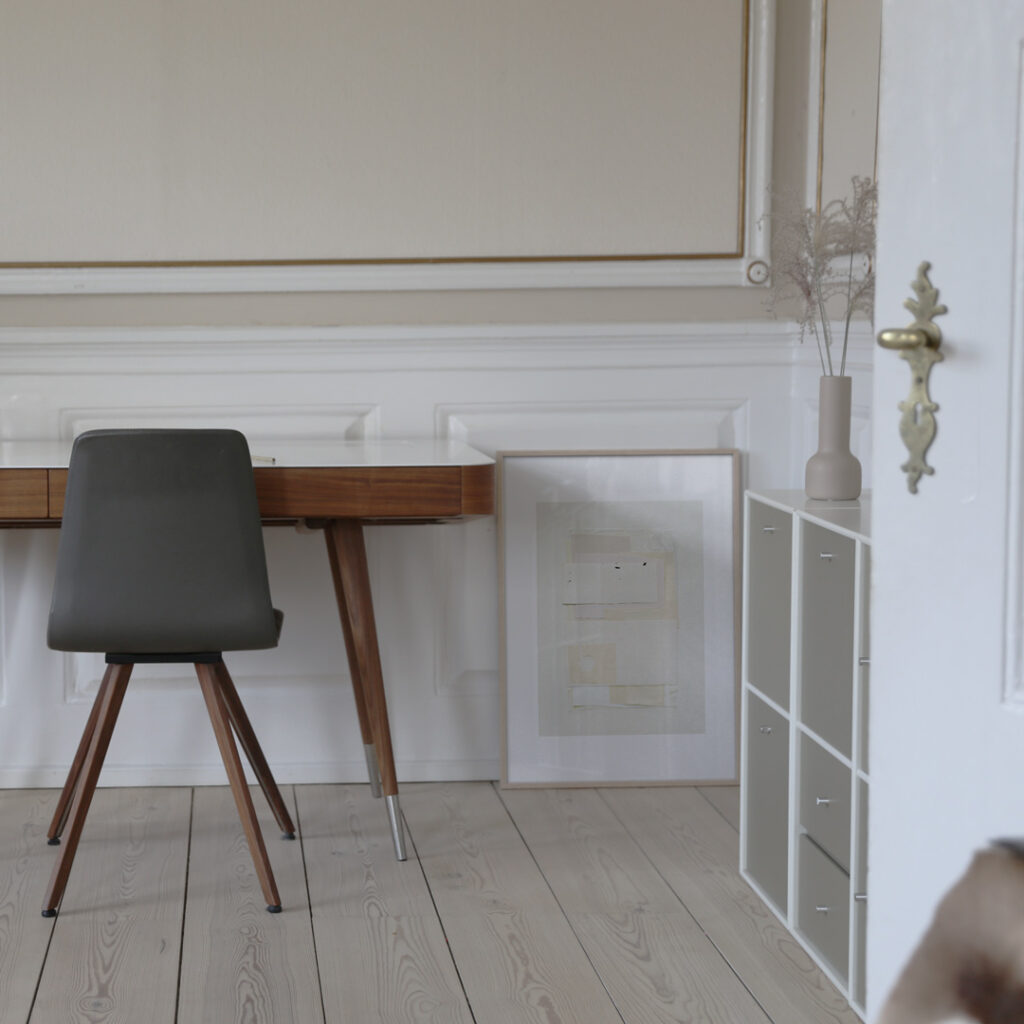 White Poem in a thin oak frame standing on the floor next to a design work table